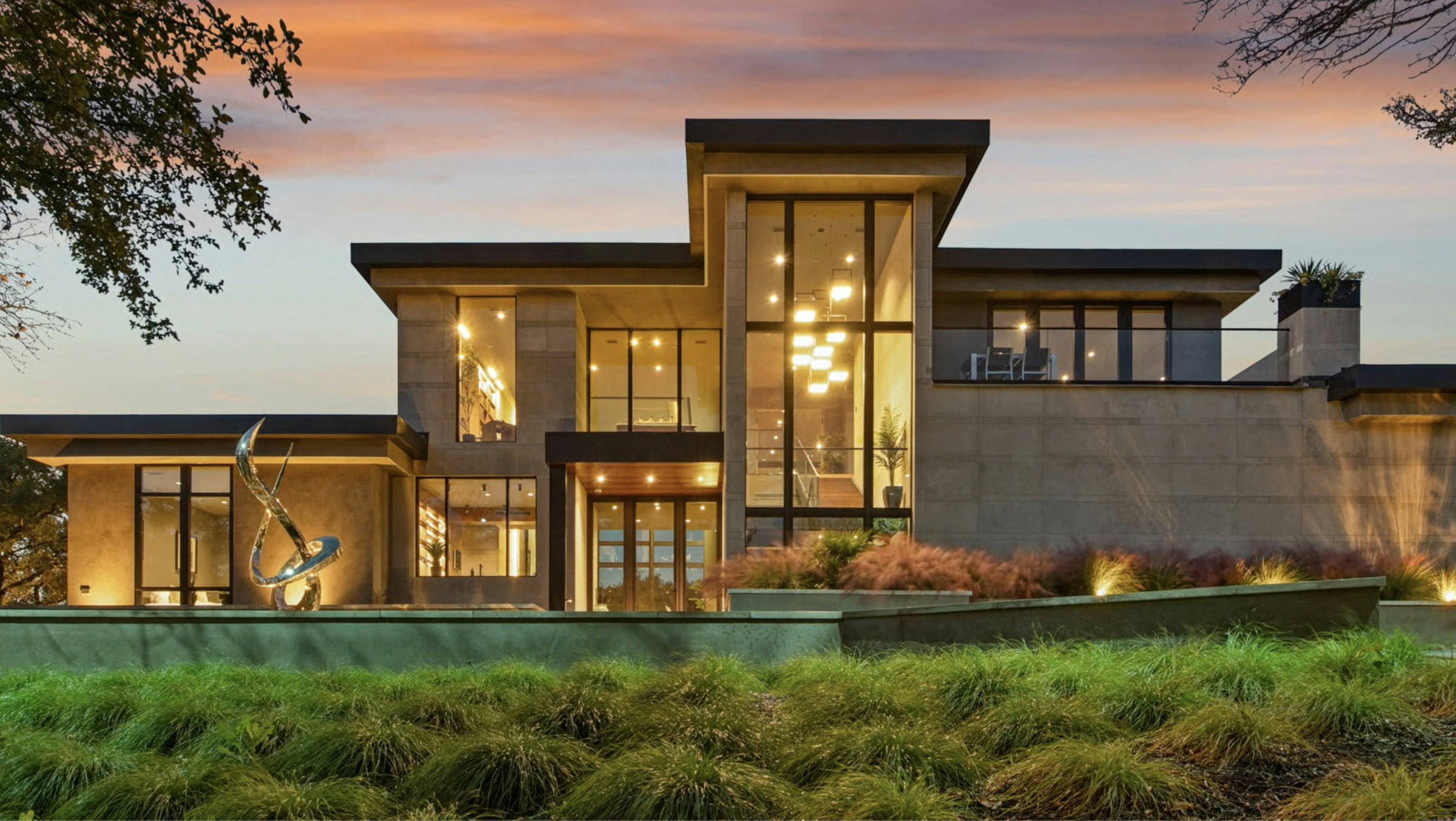 Editorial photograph: a row of mid-century modern homes in the Silicon Valley hills at blue hour, soft warm interior light glowing from windows, cool blue sky above with a single airplane contrail. A solitary figure walks a dog far in the foreground. Cinematic, restrained.